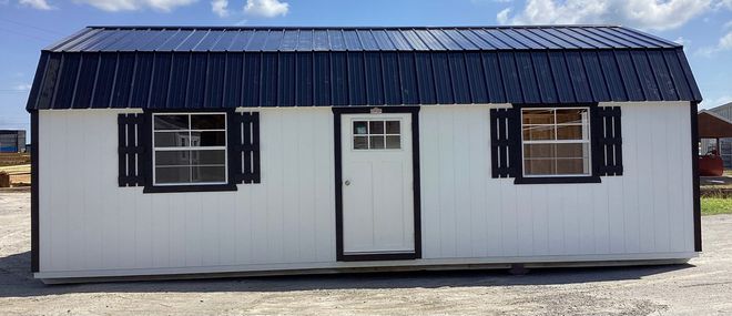 White cabin with black roof, trim, and shutters. Features a door and two windows.