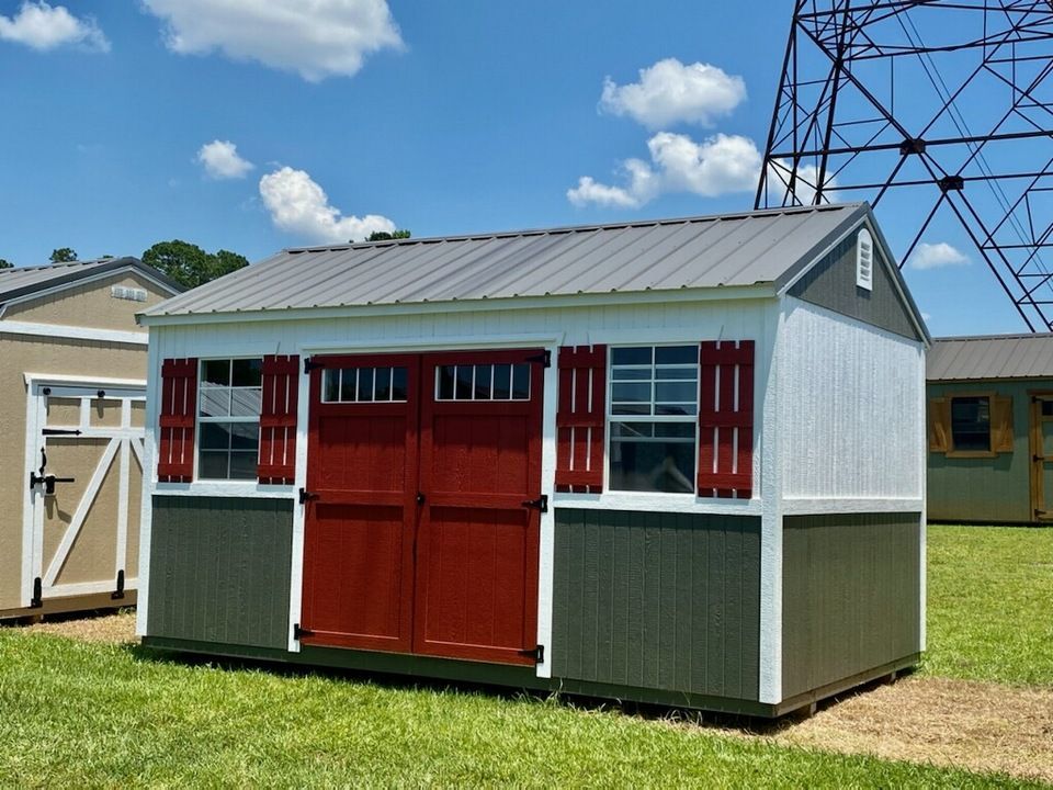 Small storage shed with red doors and shutters, gray metal roof, and green and white siding, set outdoors.