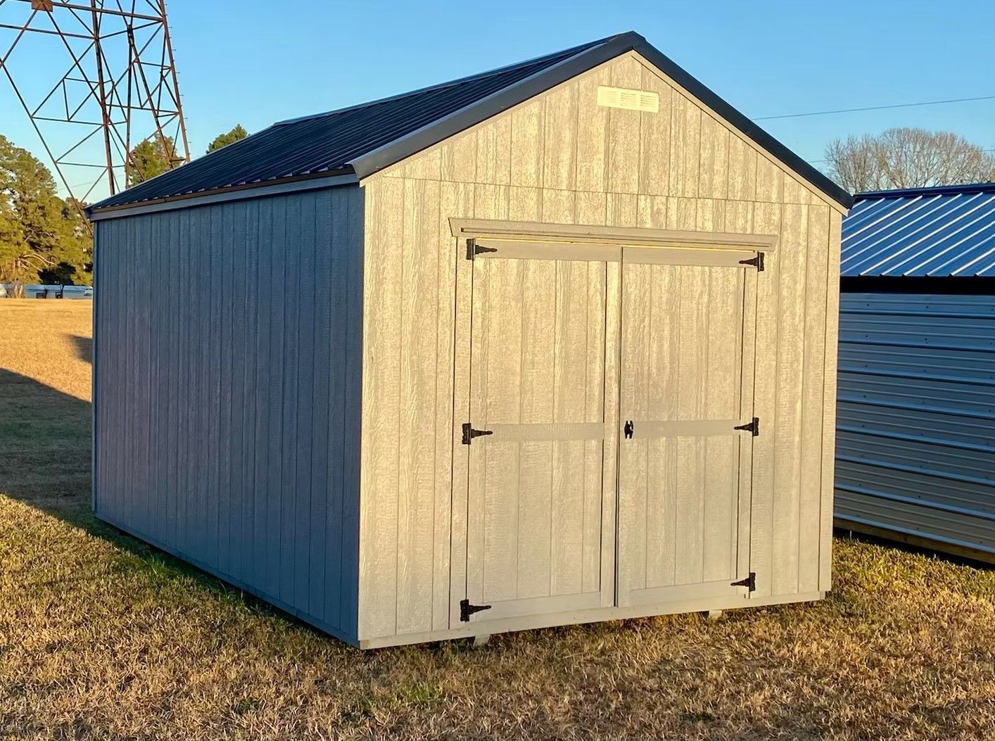 Gray shed with black roof and double doors, in a grassy field.