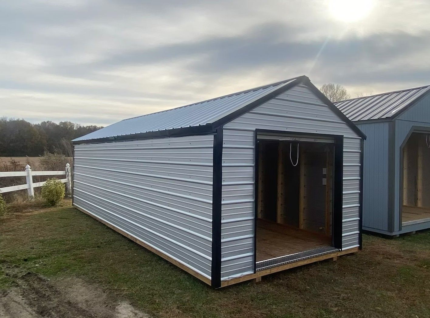 Gray metal shed with open door, sitting on a grassy lot under a cloudy sky.