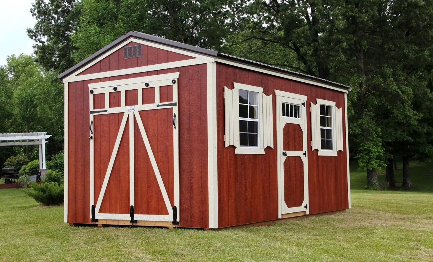 Red and white wooden shed with barn-style door, two windows with shutters, set in a grassy yard.