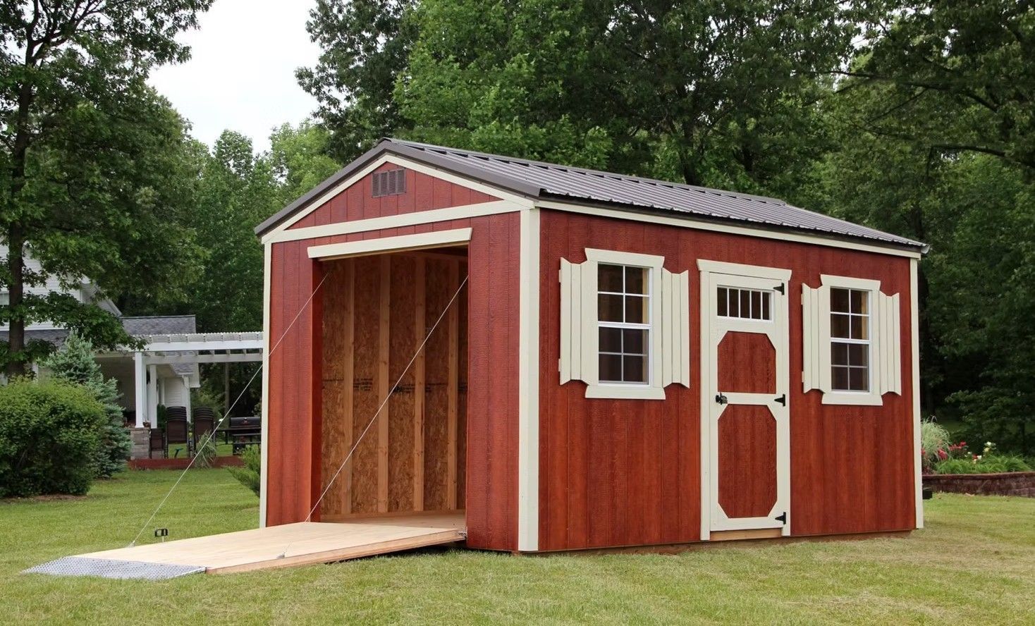 Red storage shed with an open garage door and a ramp on a grassy lawn.