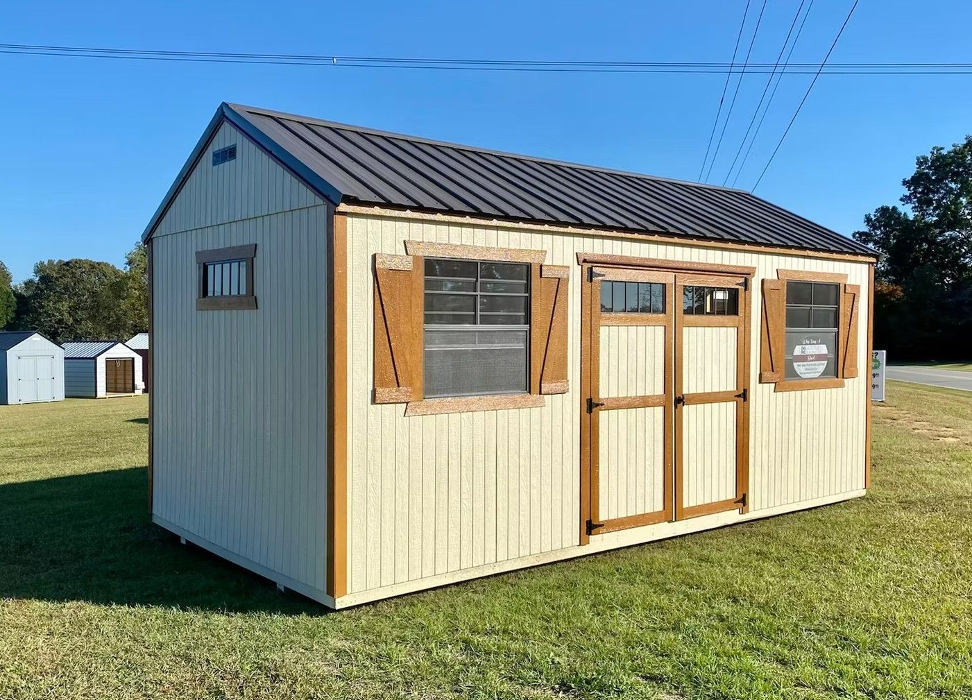 Tan shed with brown trim, windows, and doors. Brown corrugated metal roof. Located on grass.