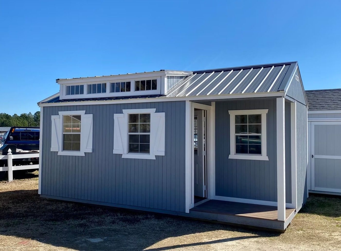 Blue shed with white trim, windows, shutters, and a small porch under a clear sky.