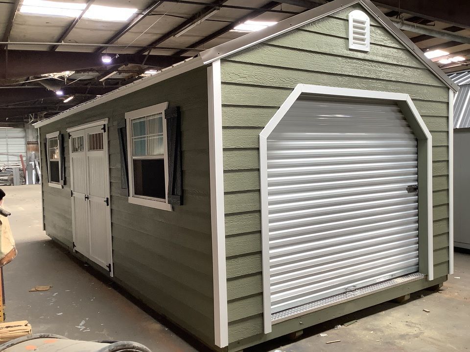 Green and white shed with a roll-up garage door, window, and shutters.