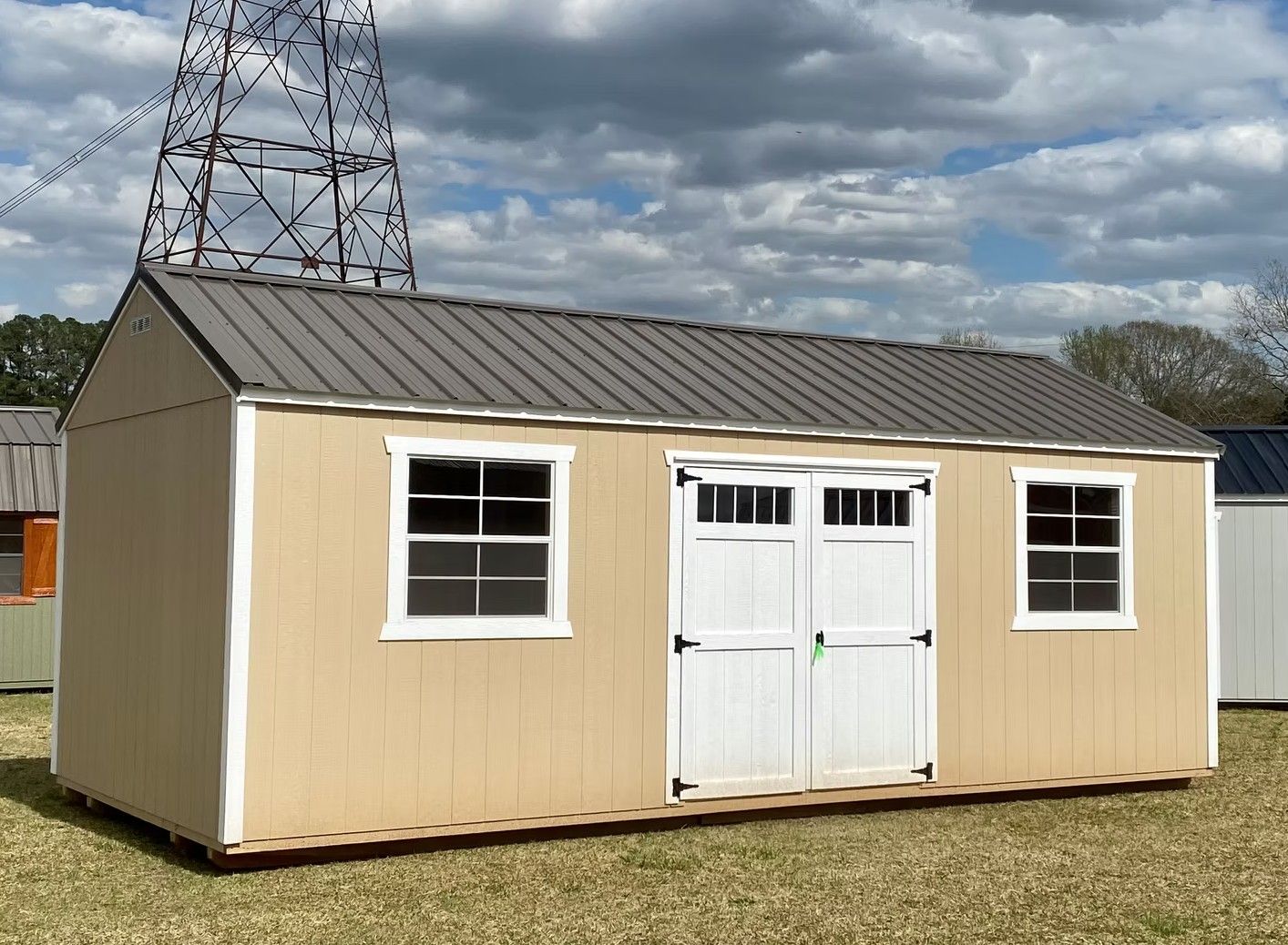 Tan shed with gray metal roof, two windows, and white double doors, outdoors.