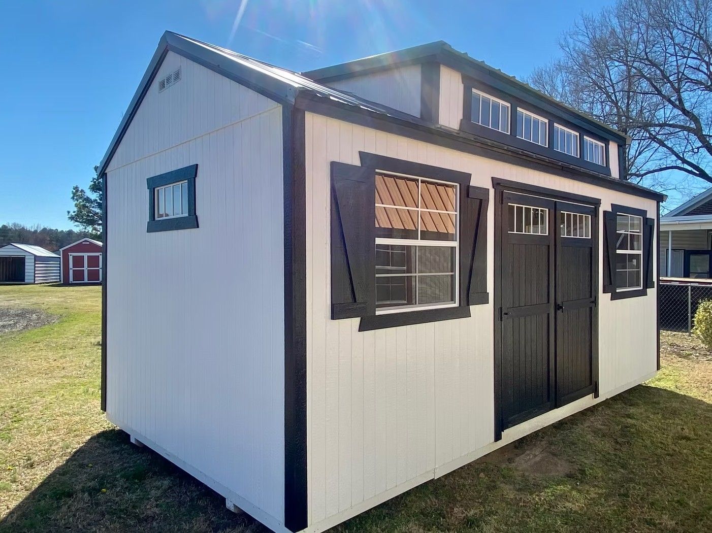 White shed with black trim and shutters, small windows, and a loft under a blue sky.