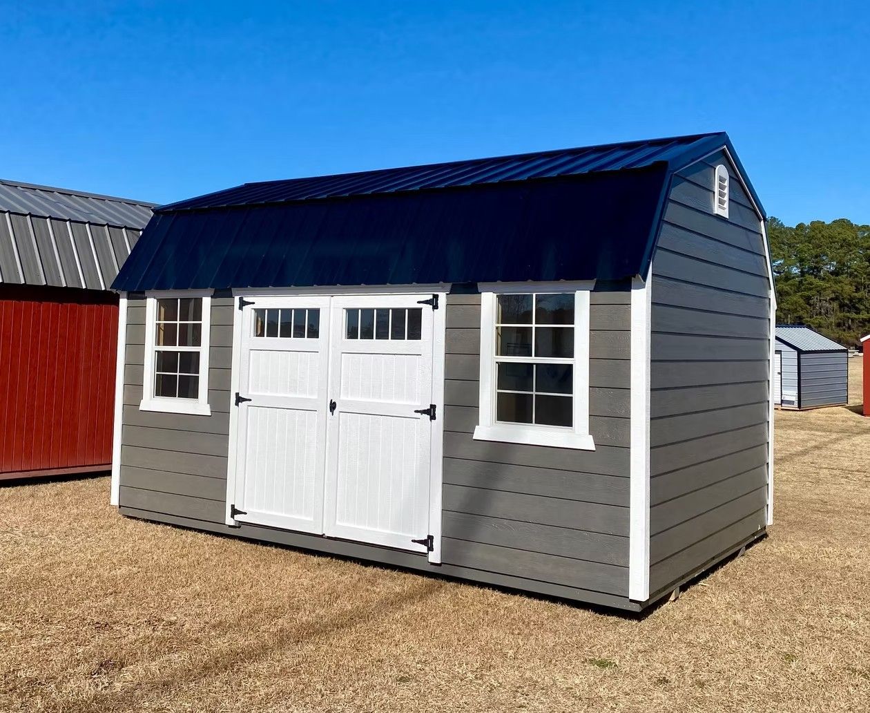 Gray storage shed with white doors and trim, blue roof, windows, and clear blue sky.
