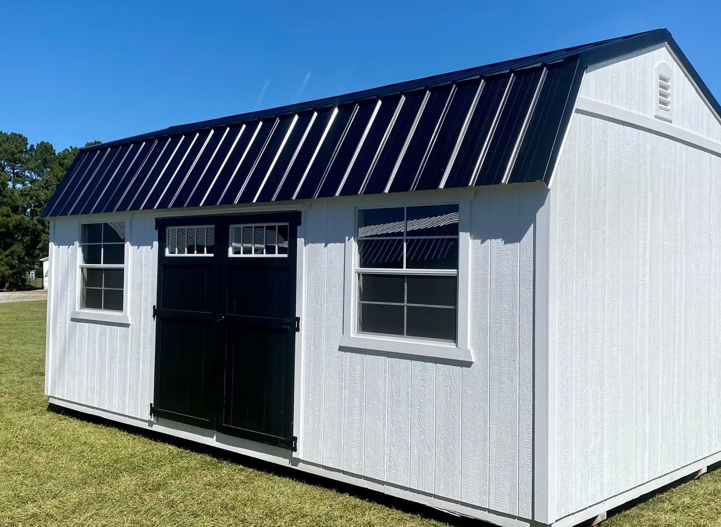 White shed with black doors and roof, windows, and clear blue sky background.