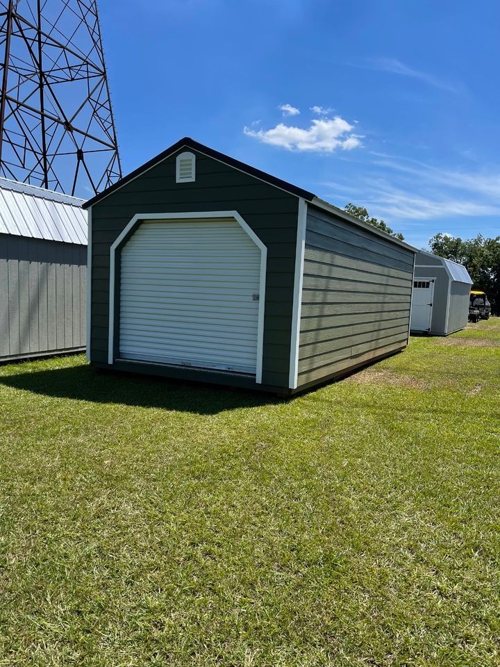 Green storage shed with a white garage door, set on grass under a blue sky.