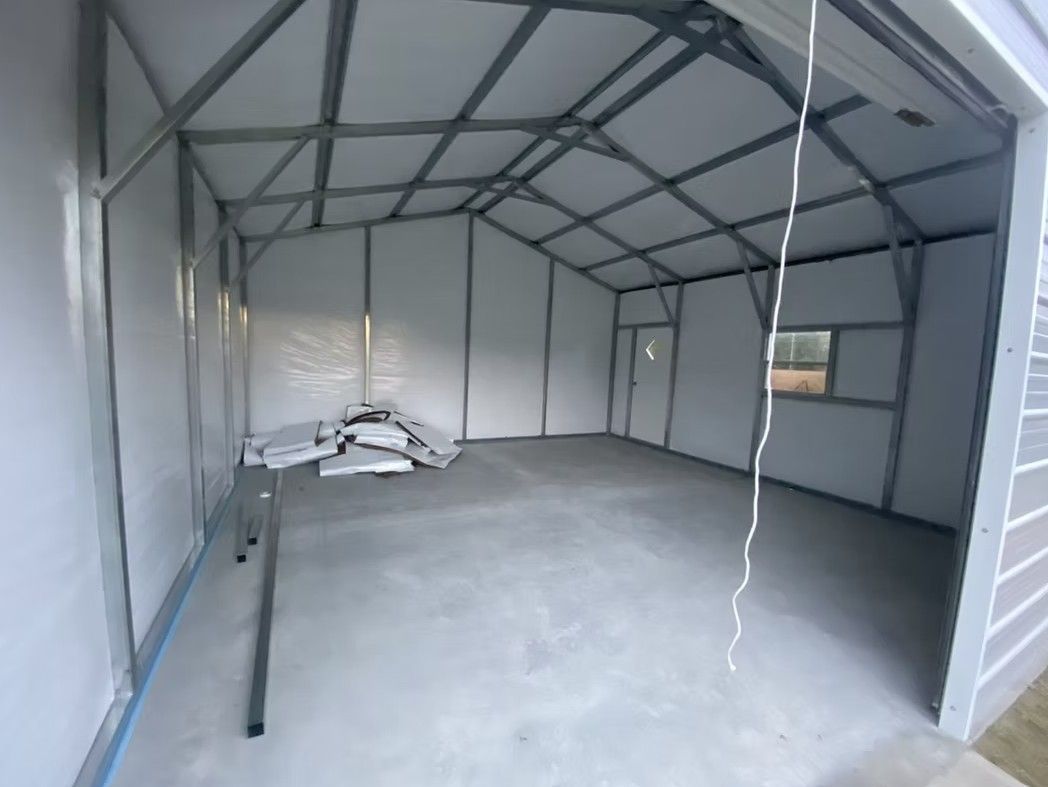 Interior view of a metal-framed building with gray walls and floor, and an open garage door.