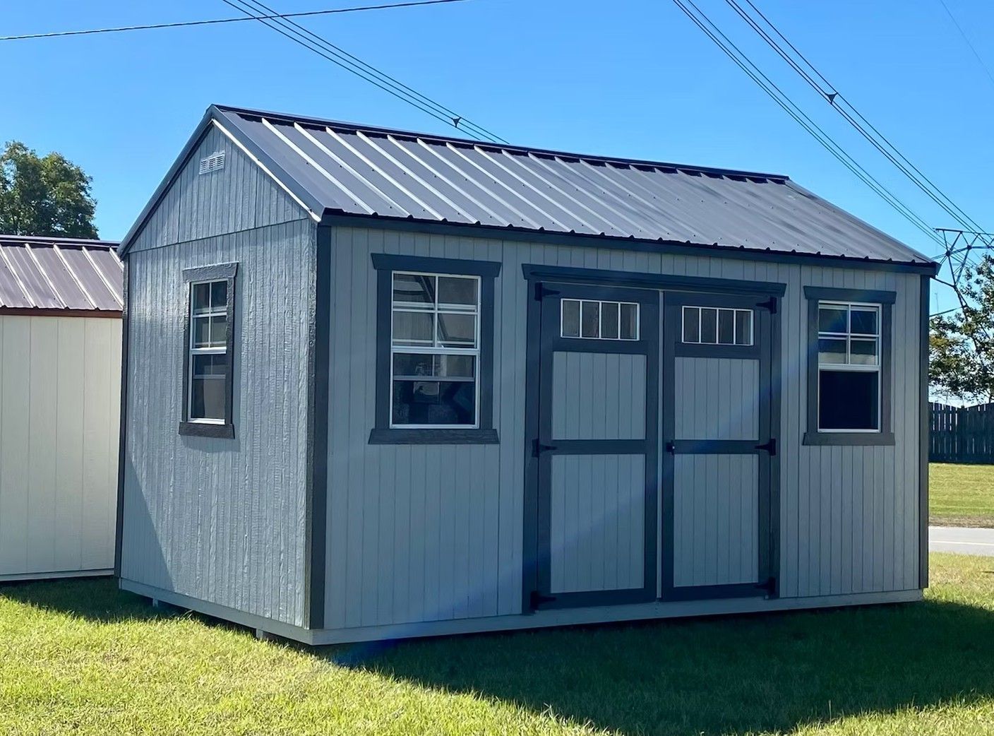 Blue shed with a metal roof, two windows, and double doors on a grassy lawn.
