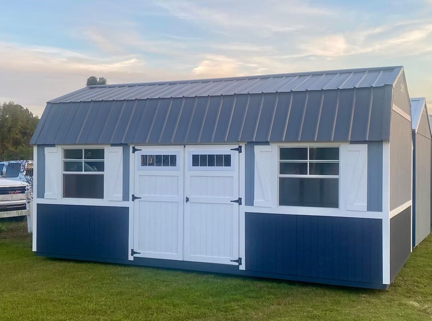 Blue and white shed with a metal roof on green grass.