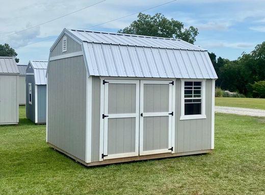 Gray shed with a white-framed door and window, metal roof, on green grass.