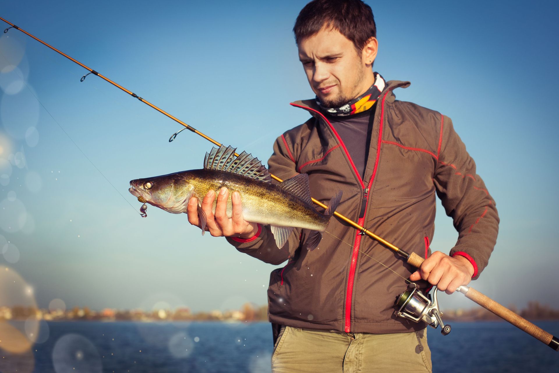Man holding a fish and fishing rod by the water at sunset