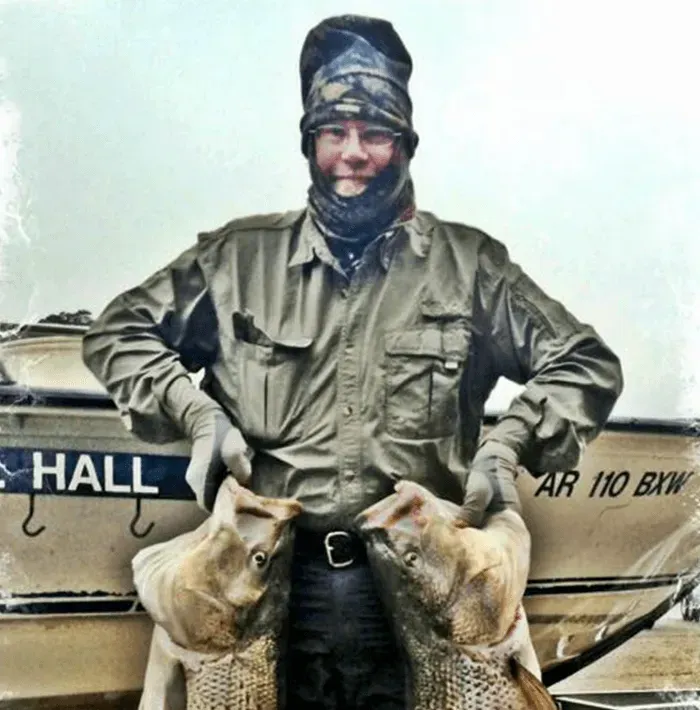 Smiling person in winter gear holding two ducks in front of a boat named Hall