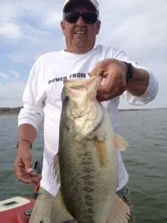Man holding a large bass on a boat with open water behind him.