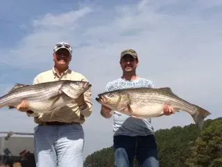 Two people holding large fish outdoors under a cloudy sky