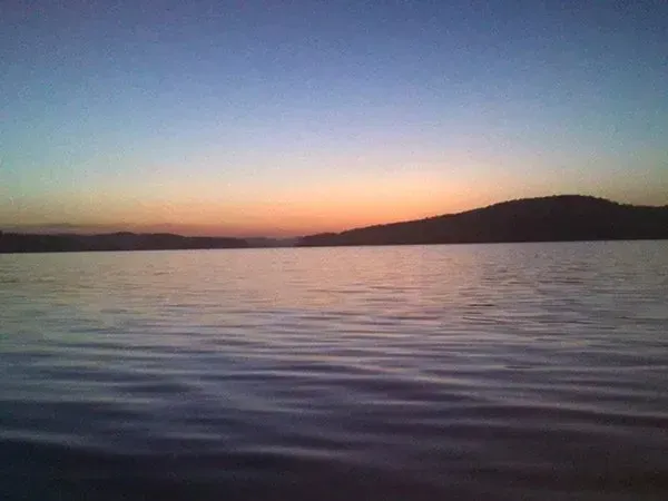 Calm lake at sunset with pink-orange horizon and dark hills silhouetted in the distance