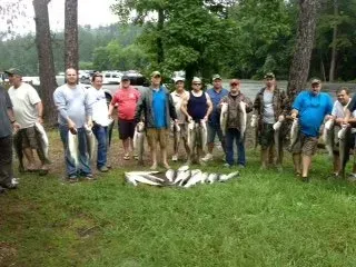 Group of people standing outdoors beside a pile of freshly caught fish on grassy ground.