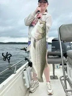 Person holding a large striped fish on a boat on a lake