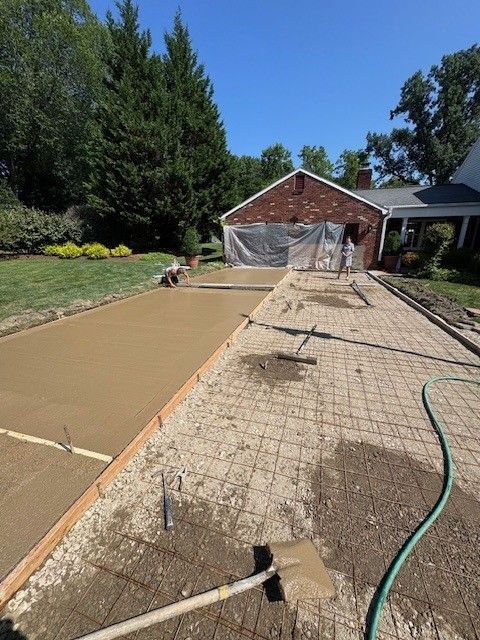 Construction of a concrete driveway. Workers are smoothing wet concrete while the unpoured section has rebar and gravel. The garage is in the background.
