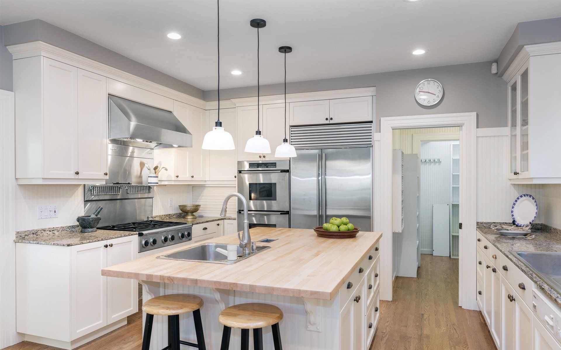 Bright white kitchen with a wooden island, stainless steel appliances, and gray walls.
