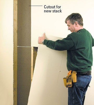 Man installs drywall, using cutout for new stack in the wall.