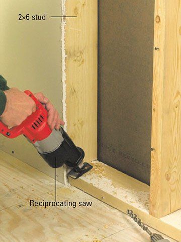 Person using a reciprocating saw to cut a wooden stud in a construction setting.