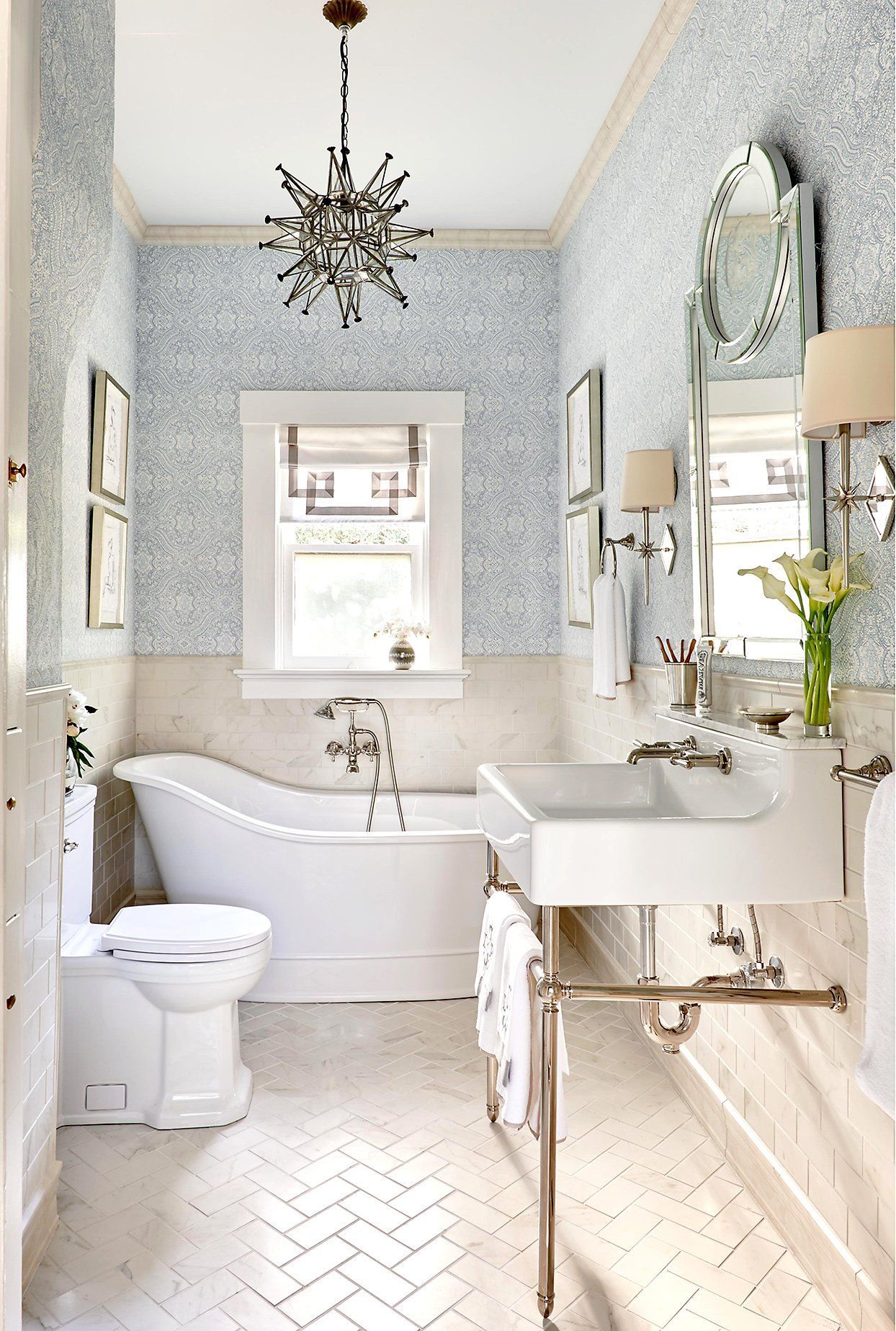 Elegant bathroom with blue patterned wallpaper, clawfoot tub, and pedestal sink.
