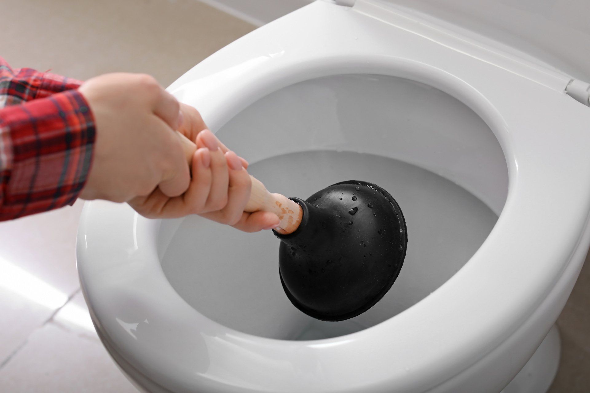 Person plunging a white toilet with a black plunger.