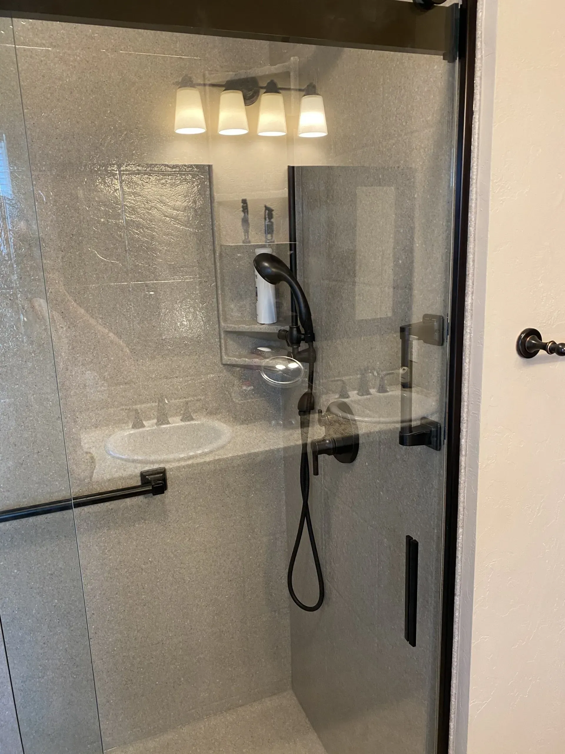 Shower stall with textured glass door, dark fixtures, and white sink.
