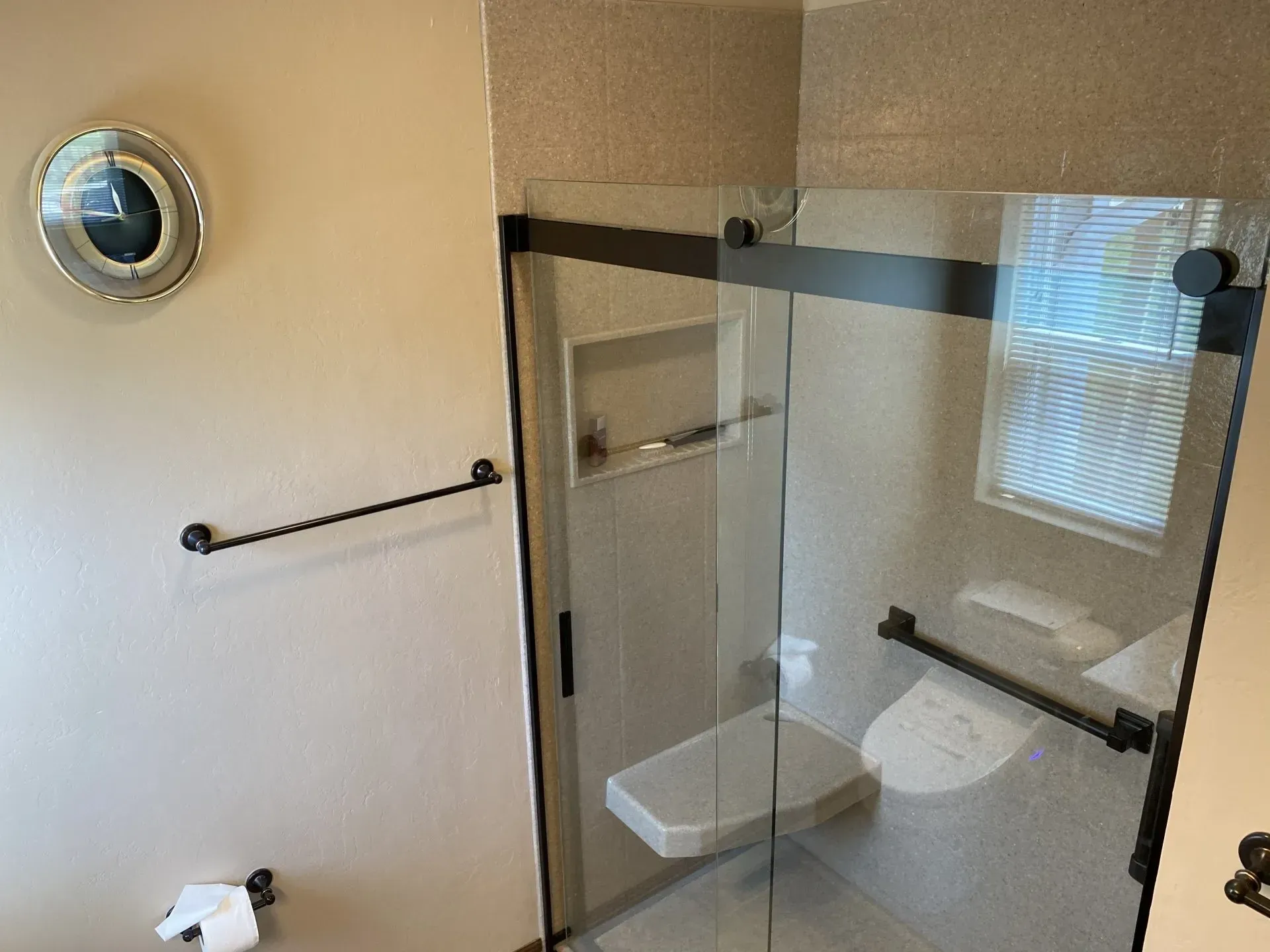 Bathroom with a glass shower enclosure, black fixtures, and a shower seat.