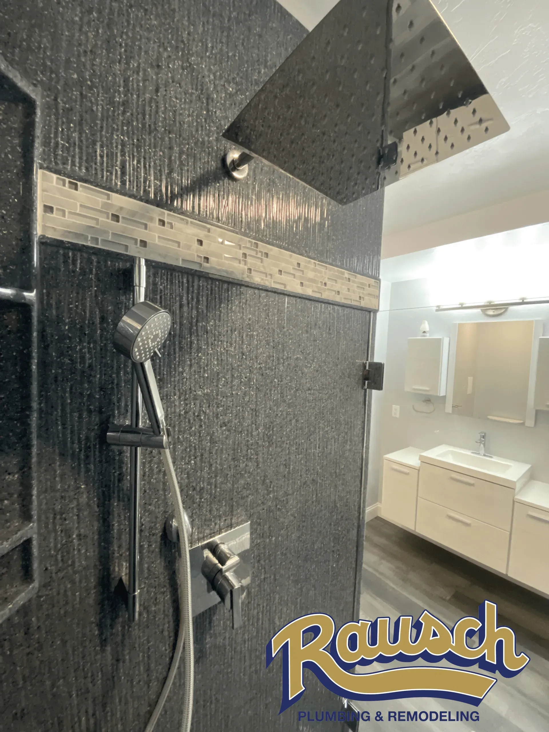 Black tile shower with rain showerhead, handheld shower, and bathroom vanity visible.