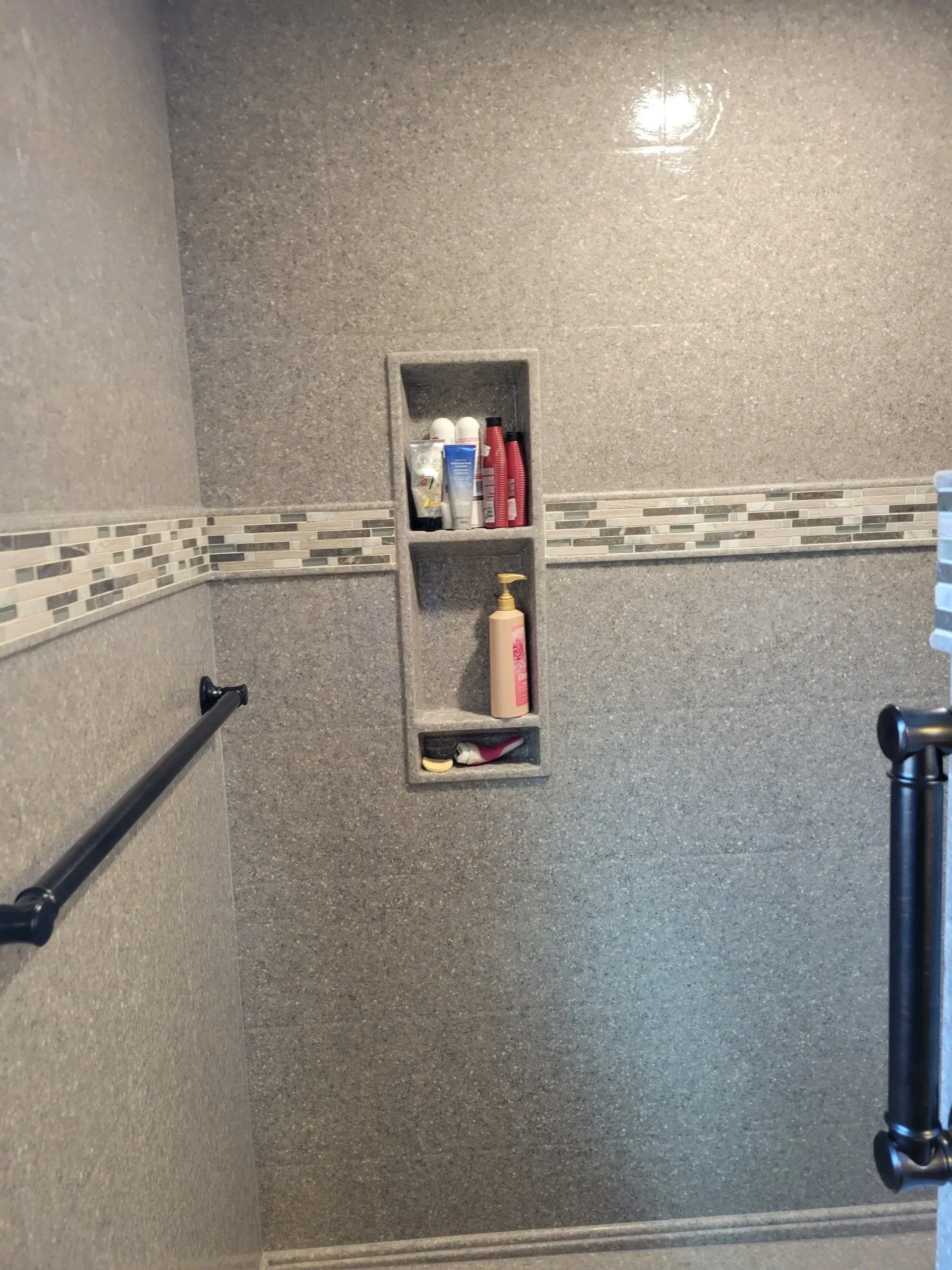 Shower interior with tiled walls, built-in shelf for toiletries, and a grab bar.