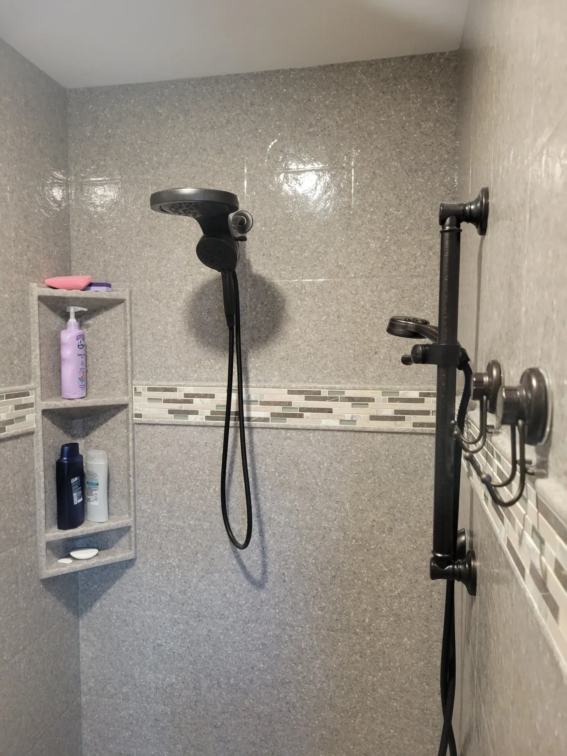Shower with gray speckled tile, shelf with products, and black shower fixtures.