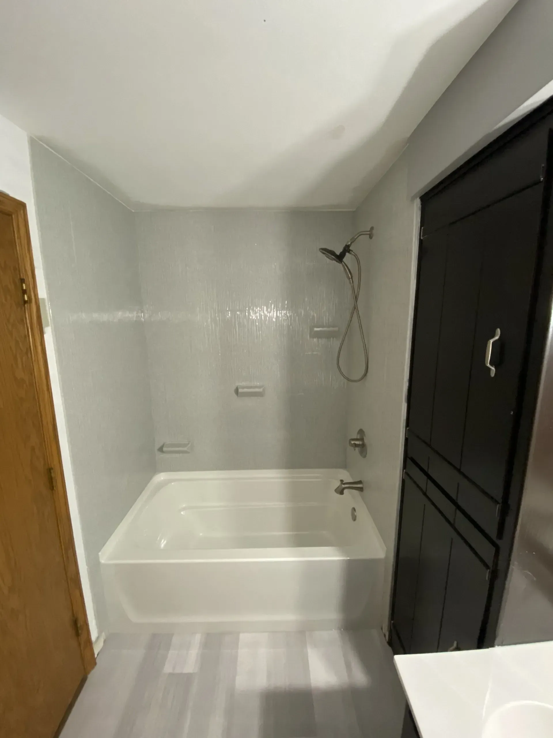 Bathroom with white tiled shower, bathtub, and black storage cabinet.