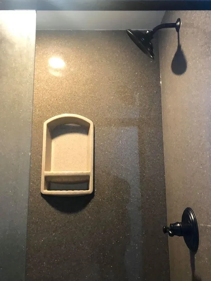 Shower stall with dark gray speckled wall, dark shower head and faucet, and a light-colored soap dish.