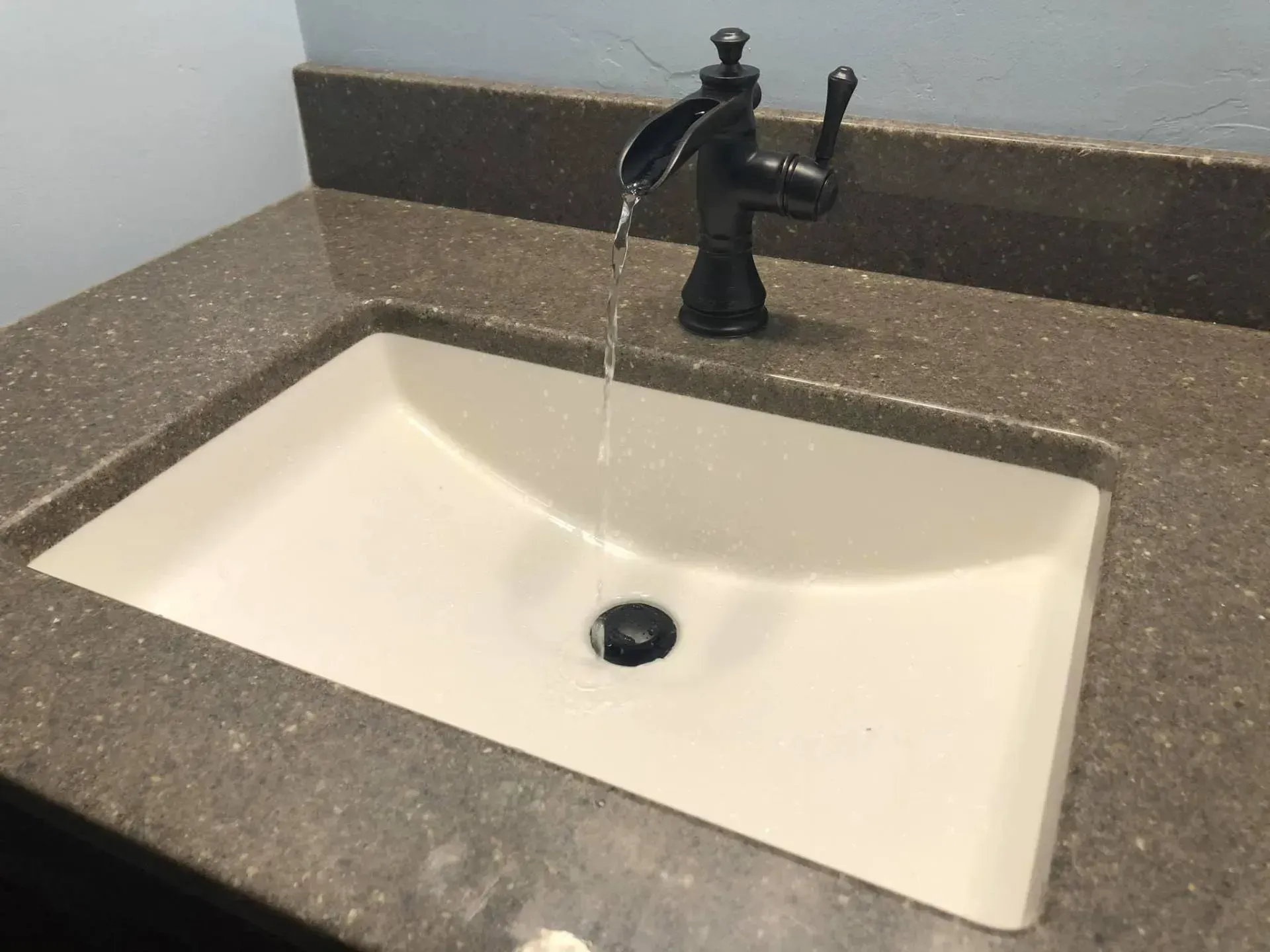 Bathroom sink with water running from black faucet into a white basin on a brown countertop.