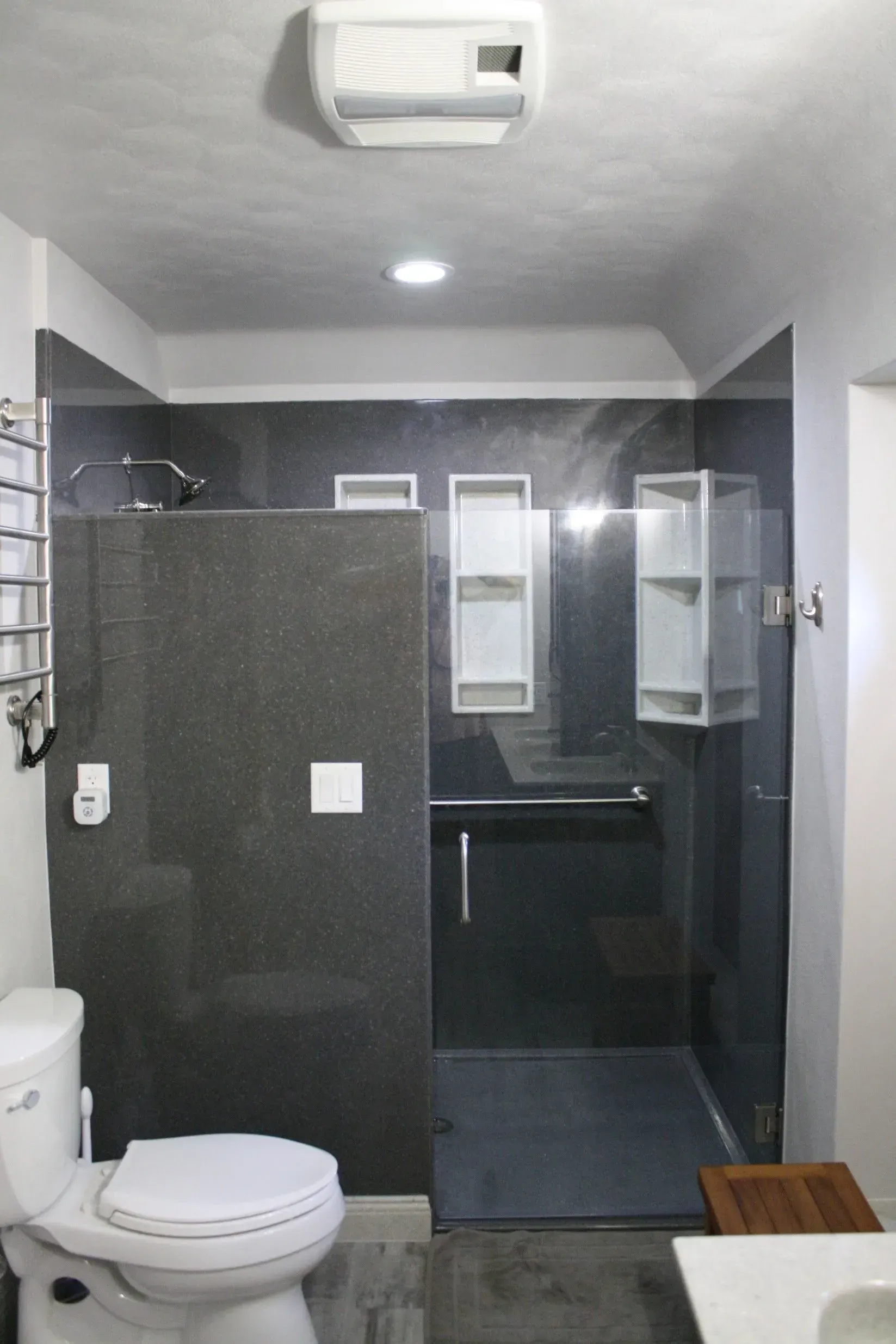 Bathroom with gray walls, glass shower, toilet, and towel rack.