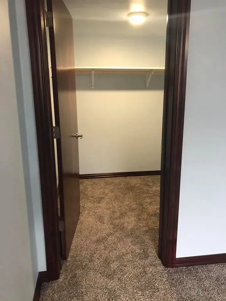 Open doorway to a closet with a shelf; dark brown trim, carpet, and white walls.