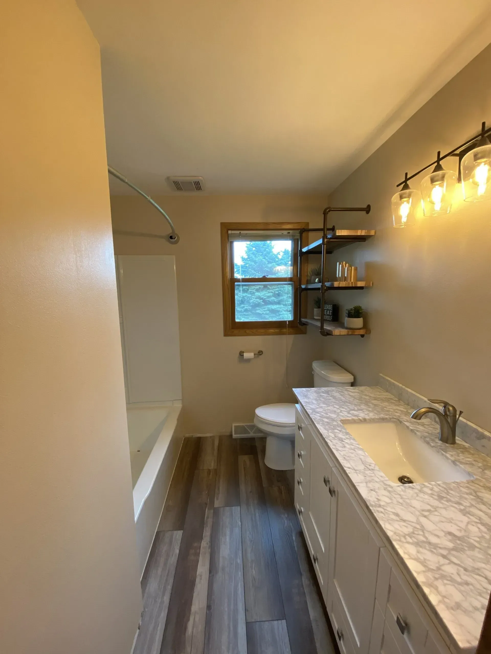 Bathroom with a white vanity, toilet, and bathtub. Wooden floors and tan walls.