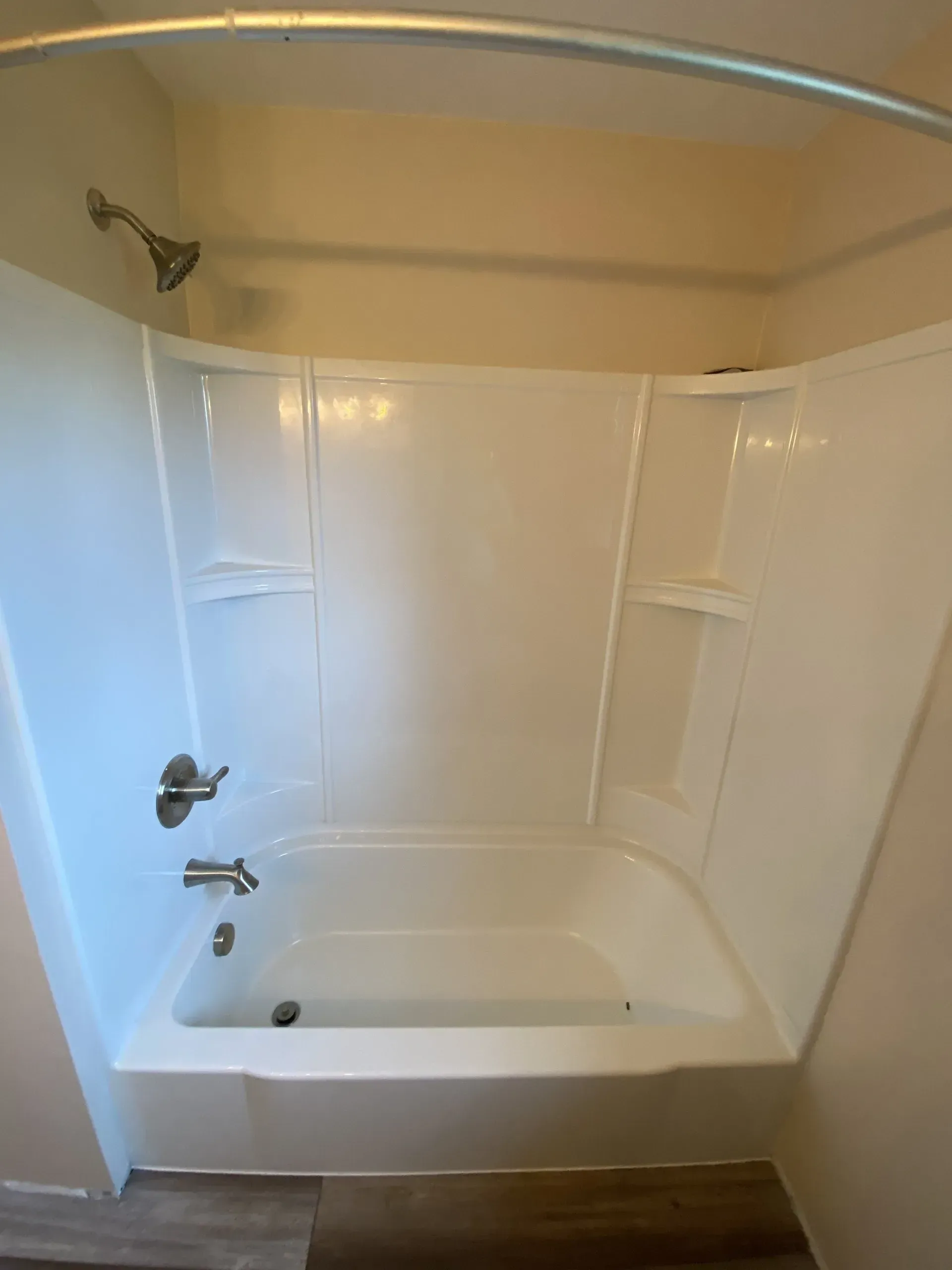 White bathtub/shower combo with curved shower rod, built-in shelves, and silver faucet fixtures.