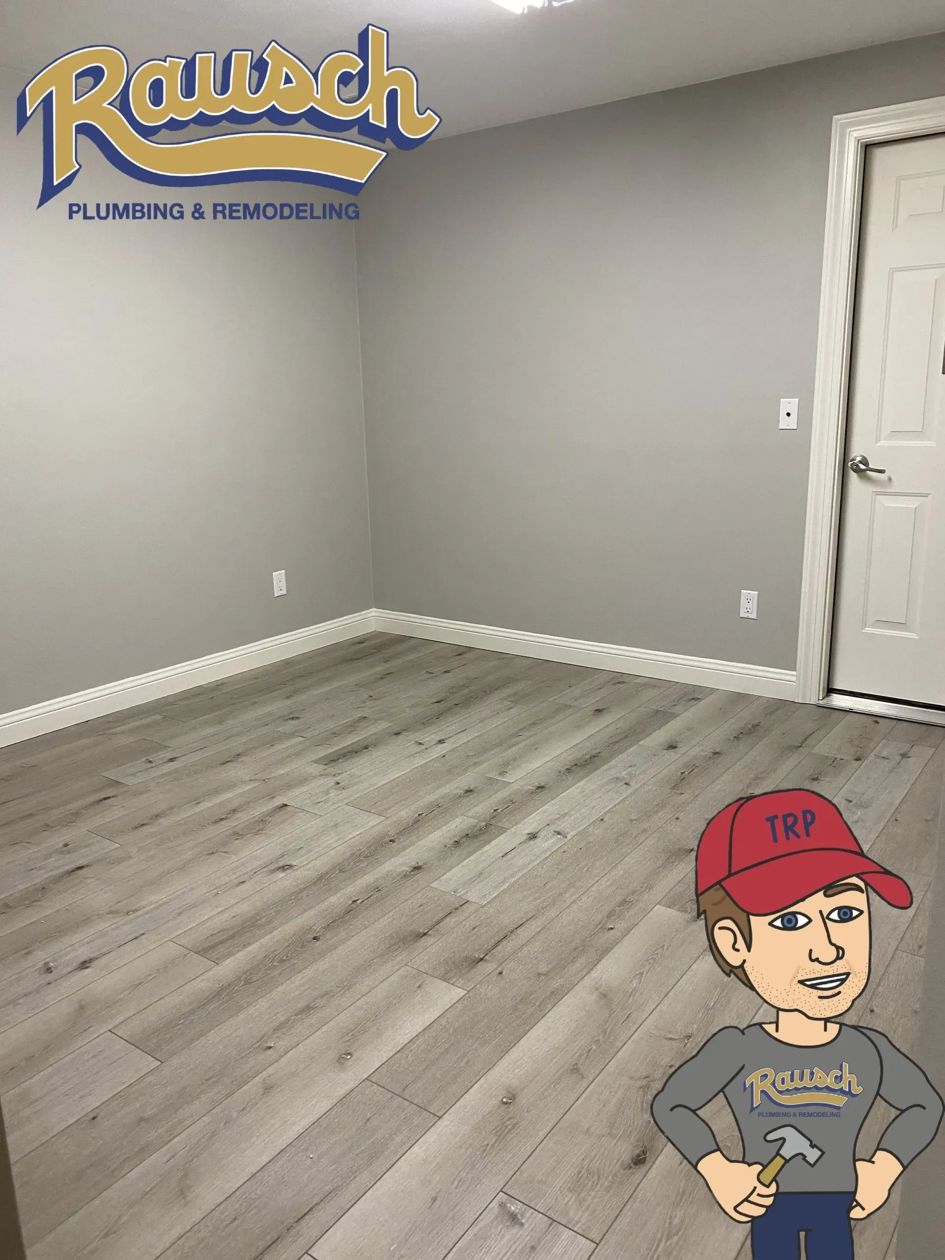 Empty room with gray walls and light wood-look flooring. Rausch Plumbing logo in corner, cartoon figure holding a hammer.