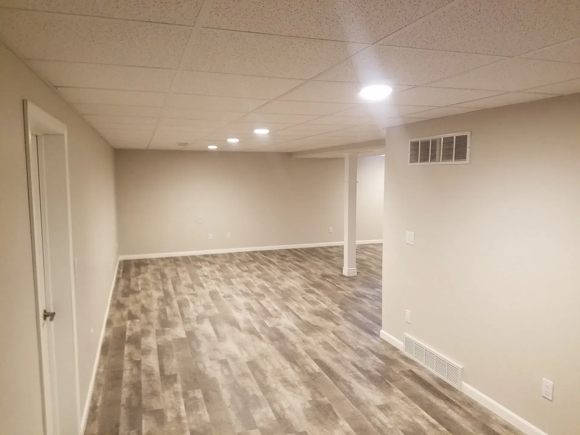 Finished basement with light gray walls, wood-look flooring, and recessed lighting.