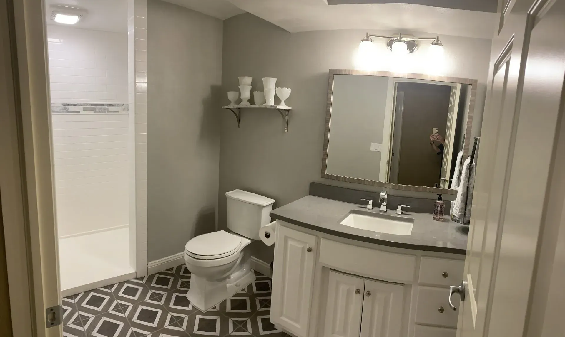 Bathroom with white vanity, gray countertop, gray walls, patterned floor, and shower.