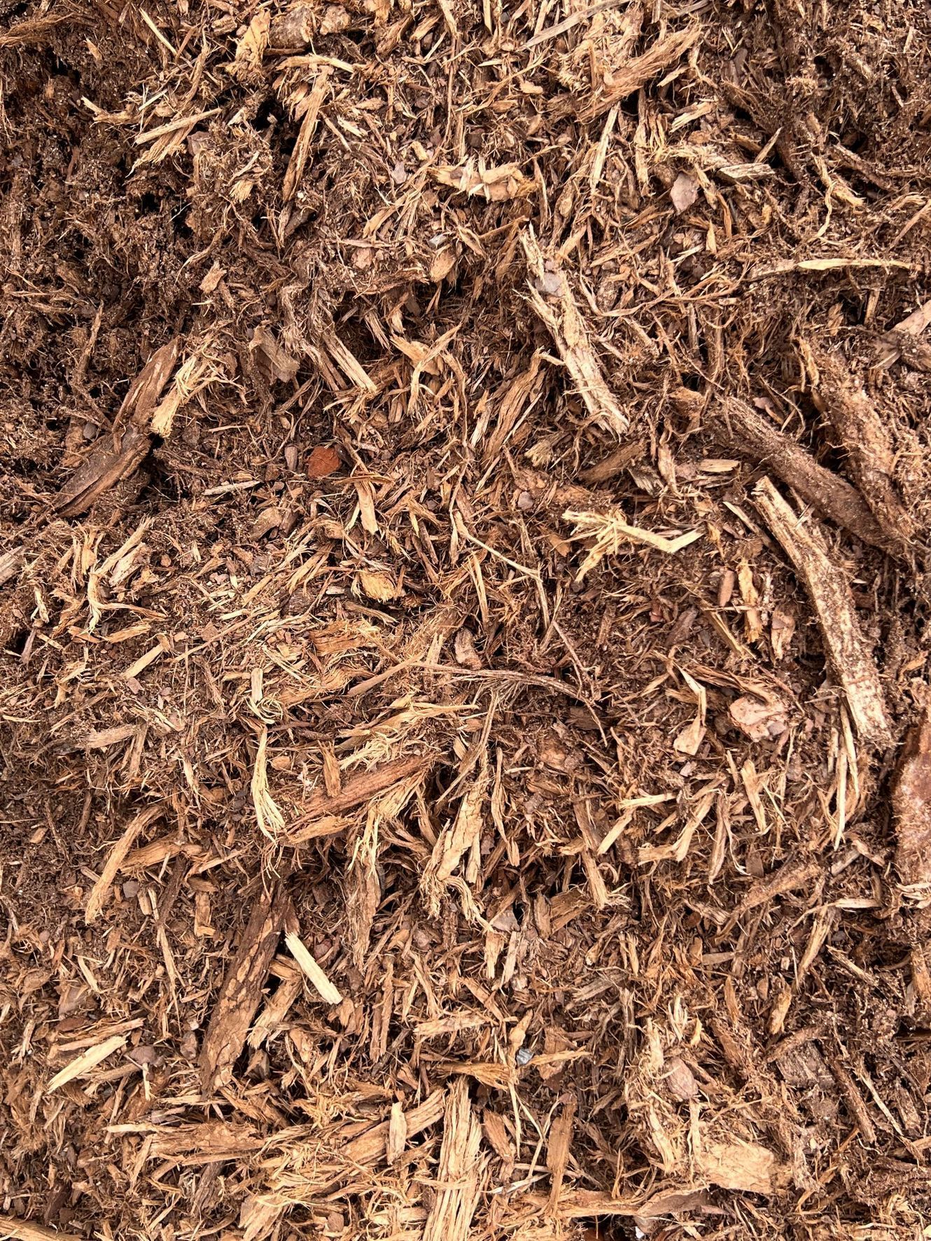 A close-up view of brown wood mulch, consisting of shredded bark and wood chips with varied textures and earthy tones.