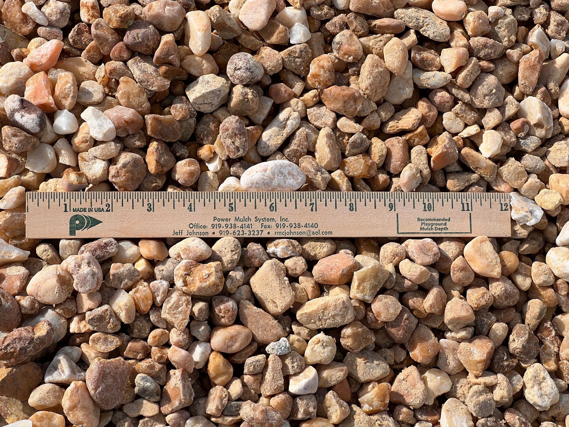 A 12-inch ruler resting on a pile of small, multi-colored beige and tan landscape gravel.