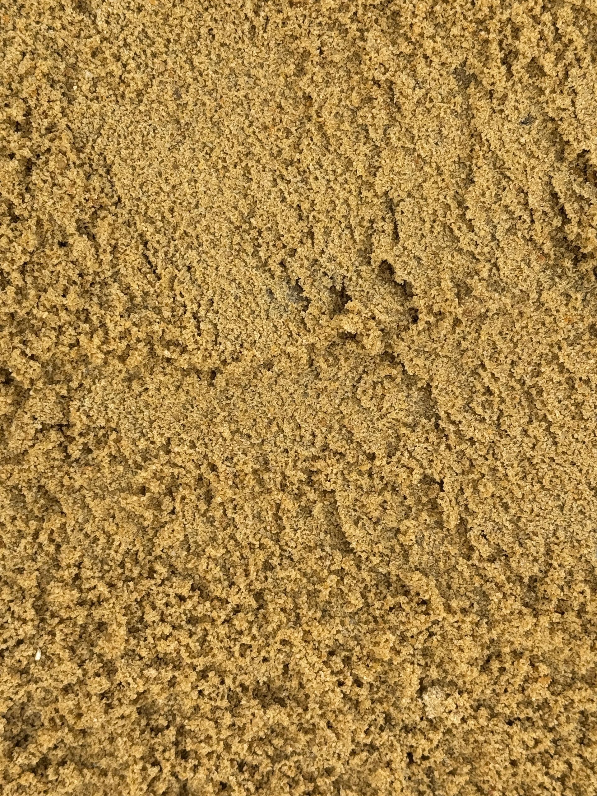 A close-up, top-down view of light brown, coarse sand with a granular, uneven texture.
