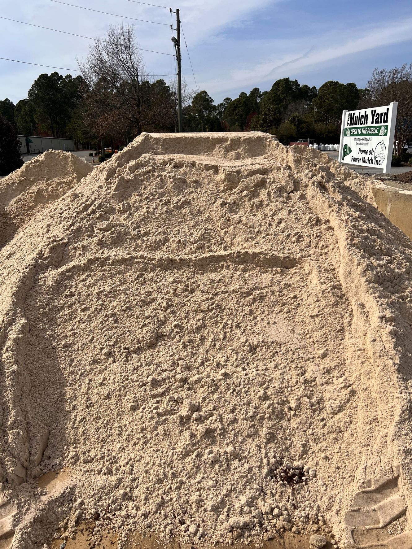 Pile of tan sand with steps, sign for mulch products in background.